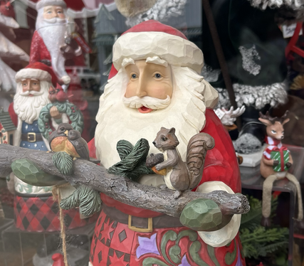 A photo of a large statue of Santa Claus in a store window; Santa is holding a tree branch with a tree squirrel standing on it.