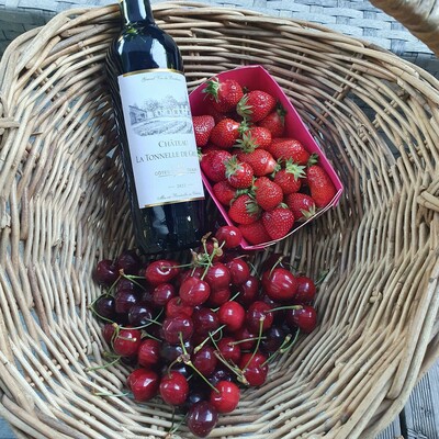 A basket with wine, cherries and strawberries.