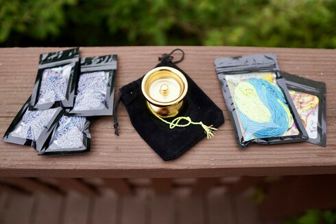 Packs of yo-yo strings and a gold plated yo-yo. The string on the left is a mix of white, blue, and pink threads. The string on the right fades from bright yellow to a soft blue. The yo-yo is a gold plated Zero by AT Design Lab. It is a fairly traditional organic butterfly shape with nice smooth curves.