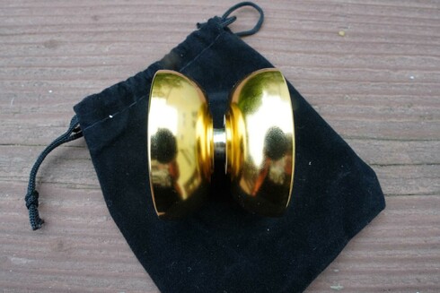 A close up view of the gold plated ZERO by AT Design Lab. It is shiny and new looking. This view shows the profile of the yo-yo, which is a rounded organic butterfly shape, and you can see the schmoove grooves on the inner walls.