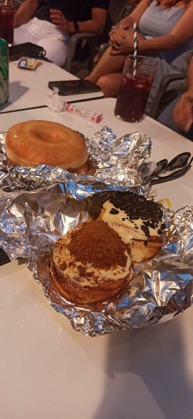 Dos donuts gigantescos y dos cinnamon rolls sobre papel albal en la mesa de una terraza