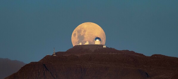 Another night of observing begins at the U.S. National Science Foundation Cerro Tololo International Observatory (CTIO) in the Chilean Andes, a Program of NSF NOIRLab, as the Moon sets below the horizon. The Moon appears massive and with a mysterious yellowish glow as it retreats behind the SMARTS–GSU 0.9-meter Telescope on the left, the SMARTS–GSU 1.5-meter Telescope in the center, and the Víctor M. Blanco 4-meter Telescope on the right. Both the SMARTS-GSU telescopes are operated by the Georgia State University Research Foundation.