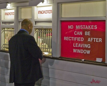 Photograph of a man in a suit standing at a sales window. A sign on the wall beside him says "NO MISTAKES CAN BE RECTIFIED AFTER LEAVING THE WINDOW".