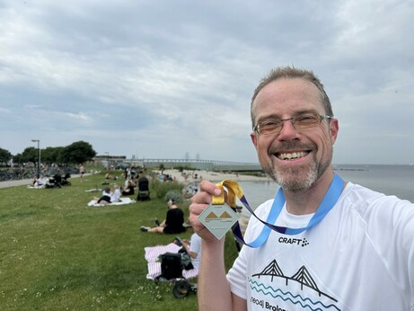 Me near Malmö. Holding up the medal for the Bridgerun. Öresund bridge visible in the back.