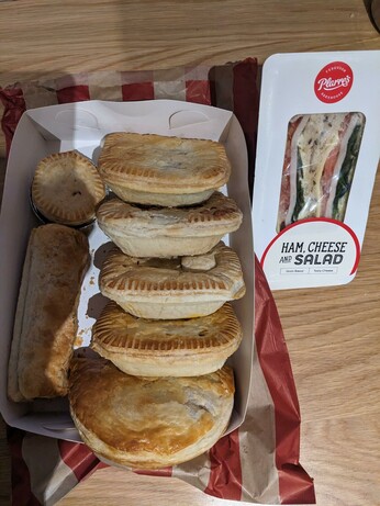 Ham, Cheese and Salad sandwiches in a tri cut box, and in a large white pastry box sits 4 X unknown pies, a pastie, a sausage roll and mini pie.