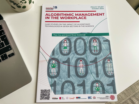 Picture of my desk, on the left a bit of my silver coloured notebook, in the back a large coffee mug with green dots, in the centre a printed publication titled Algorithmic management in the workplace, case studies on the impact of algorithmic technologies in seven sectors in the nordics, by Theo cox and Gerard rinse oosterwijk.