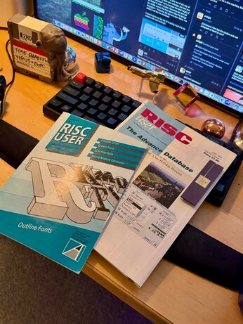 Two RISC User magazines lying on a desk, on the keyboard of a computer setup