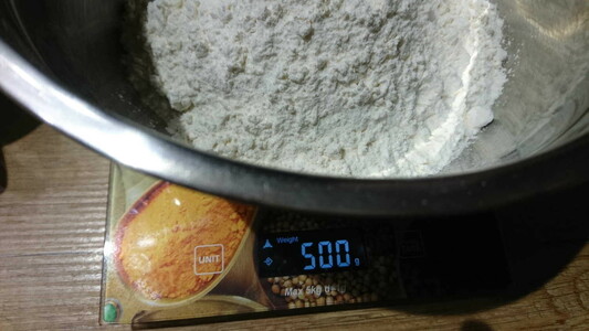 A steel bowl with flour on a kitchen scale. The display shows 500 g.