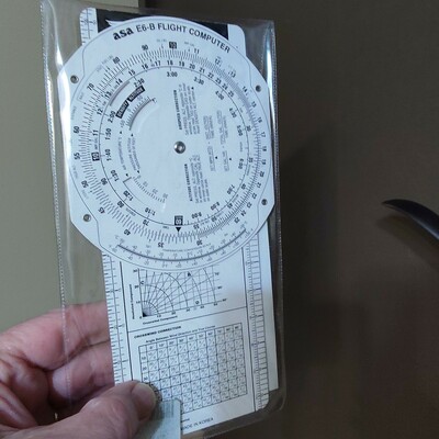 A circular slide rule made of paper in a clear plastic case.