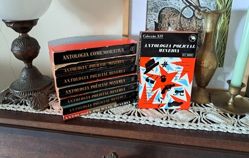 A stack of books in black and red in a writing desk with a lamp a candle a vase