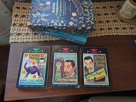 The three mentioned books with colourful covers over a table next to other books and a cup