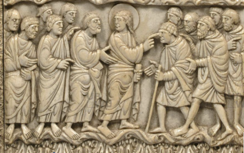 Carved yellowish ivory depicting two groups of people in flowing robes. The central figure on the left has a halo and appears to be poking the right index finger into the right eye of the central figure on the right.