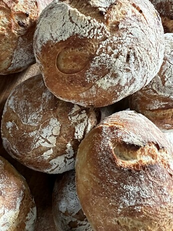Auf einem dunklen Holztisch liegt ein Holzbrett. Darauf liegen zahlreiche frisch gebackene Brötchen mit rustikalem Ausbund