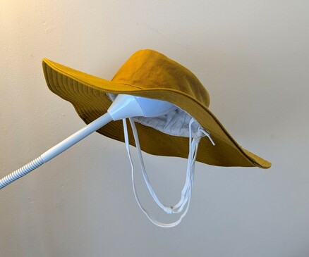 Mustard-yellow sun hat with a wide brim and a white tie string, perched on the end of a spotlight lamp arm