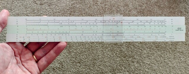 I am holding a slide rule which is about 12 inches long. Lots of scales on the top, middle and bottom sections. The middle section can slide left and right and the is a clear bit with vertical lines that slides over all 3 sections.