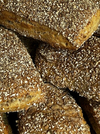 Auf einem dunklen Holztisch liegt ein Holzbrett. Darauf liegen zahlreiche frisch gebackene Brötchen mit rustikalem Ausbund.