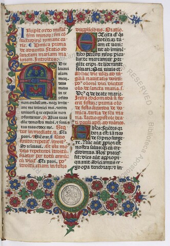f.1r from Urb.lat.109.  It is two columns of printed gothic text, with many of the lines in red, with italian borders on top, bottom and right.  There are large illuminated capitols in both columns, and an empty rondel at bottom for a coat of arms.  The library has put their ownership stamp in the middle of this rondel