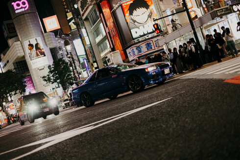 angled photo of a Nissan Skyline driving on the Shibuya crossing by night