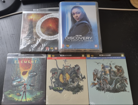 4 Bluray boxes laid out on a dark desktop. The first box is the Lord of the Rings trilogy in 4K, bot theatrical and extended versions. The complete Star Trek Discovery series in HD, The Fifth Element movie in 4K, the Jurassic Park trilogy in 4K, and the Jurassic World trilogy also in 4K.