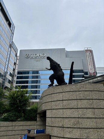The Godzilla statue shown at yet another angle, with the Toho headquarters building shown in the background. The smallish office building has a sign on it that reads TOHO - Screen & Stage - Since 1932 - Hibiya.