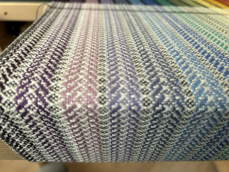 Looking at a length of woven spiral twill cloth curving around the front beam of a hand loom