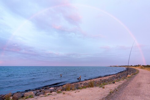 photos showing a rainow over the beach at the baltic sea. A black GFK anatenna mast is visible on the right side on the beach also and a light house far away too.
