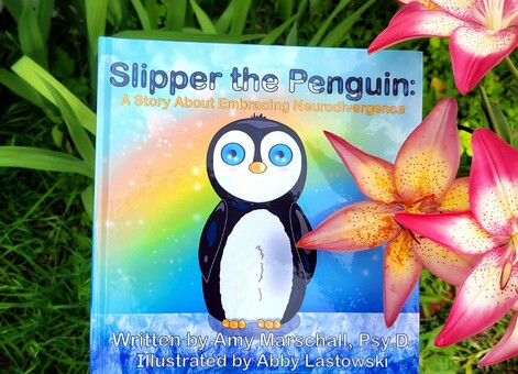 Photo of a children's book written by Amy Marschall Psy. D. and illustrated by Abby Lastowski (aka me). Featured is a super adorable penguin named Slipper who smiles because you know you want to buy this book. She is on top of ice with a sparkly rainbow behind her. 
The physical background is grass and pink and yellow lilies from Abby's garden.