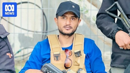 Yasser Abu Shabab wears a combat vest and holds a rifle as he sits and poses for a picture.