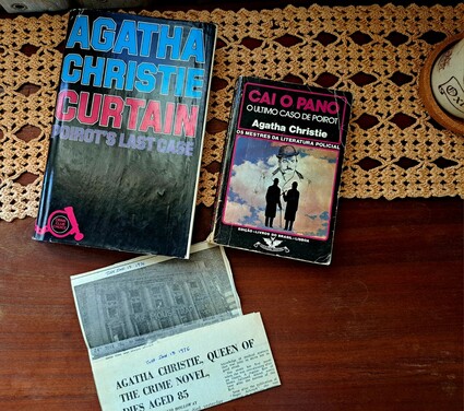 The image features a collection of items on a wooden table, covered with a beige crocheted table runner. On the left, there is a hardcover book titled "AGATHA CHRISTIE CURTAIN POIROT'S LAST CASE" with a predominantly black cover and blue and red text. The book shows signs of wear, with a slightly bent spine. To the right, there is another book titled "CAI O PANO O ULTIMO CASO DE POIROT Agatha Christie" with a black cover and a colorful illustration of two silhouetted figures against a cloudy sky. The text on the cover is in Portuguese, indicating it is a Portuguese edition. Below these books, there is a newspaper clipping with the headline "AGATHA CHRISTIE, QUEEN OF THE CRIME NOVEL, DIES AGED 85," dated June 13, 1976. The newspaper is partially visible, showing a black and white photograph of a building. The overall arrangement suggests a nostalgic display of Agatha Christie's work, including a book from her final Poirot novel and a newspaper marking her passing.

Provided by @altbot, generated privately and locally using Ovis2-8B

🌱 Energy used: 0.255 Wh