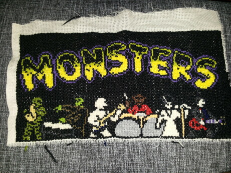 Cross stitching, the top says Monsters and below it, Creature of the Black Lagoon is playing saxophone, Frankenstein's Monster is playing the keyboard, the Mummy on bass, the werewolf on drums, Bride of Frankenstein is singing and Dracula on guitar