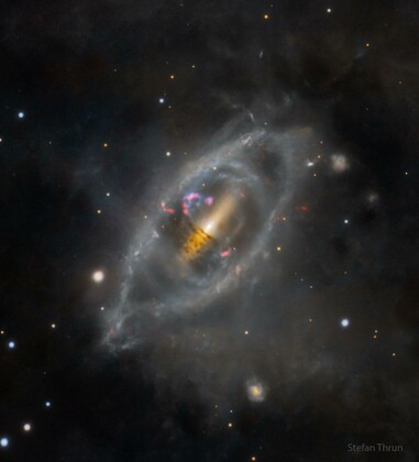 A spiral galaxy with a tilted ring of stars and gas wraps around it like a twisted ribbon. The main disk of the galaxy is flat and dark, while the ring appears lighter and loops around it at an odd angle. Faint star clouds and dust lanes extend outward, set against the blackness of space.