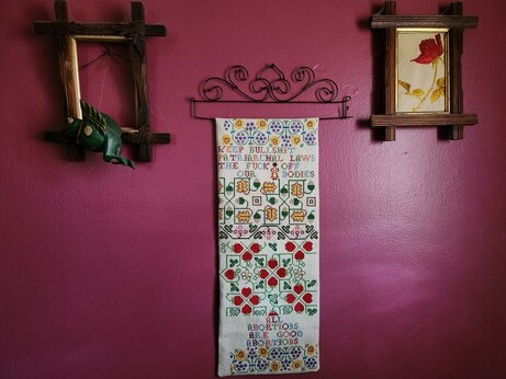 An ornate counted cross-stitch sampler hanging from a curvy black metal hanger

Amidst the designs of flowers, acorns, strawberries, etc. are the words:
"KEEP BULLSHIT PATRIARCHAL LAWS THE FUCK OFF OUR BODIES" and "ALL ABORTIONS ARE GOOD ABORTIONS."
