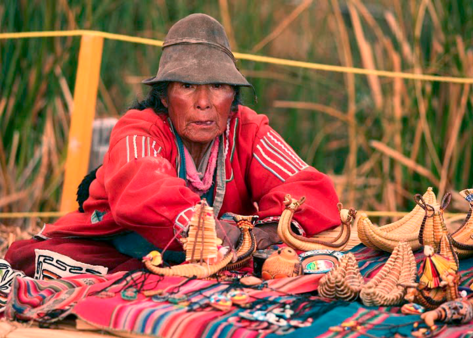 Photo of an indigenous south american man selling handmade wares at a table with a colorful native woven cloth.