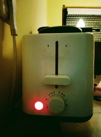 The light is on on the toaster, inside of which toast is toasting, round side down.