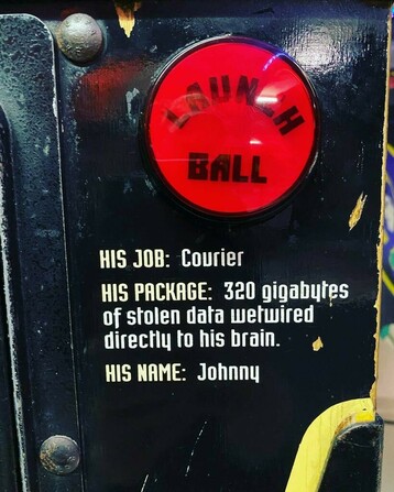 Closeup of Johnny Mnemonic pinball machine's ball launch button. Under the red button that says "Launch Ball" reads:

His job: Courier
His package: 320 gigabytes of stolen data wetwired directly to his brain
His name: Johnny