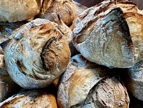 Auf einem dunklen Holztisch liegt ein Holzbrett. Darauf liegen zahlreiche frisch gebackene Brötchen mit rustikalem Ausbund