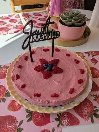 A pink cheesecake decorated with fresh raspberries and a couple of blueberries. There's also a black acrylic cake topper on it that says "just married"