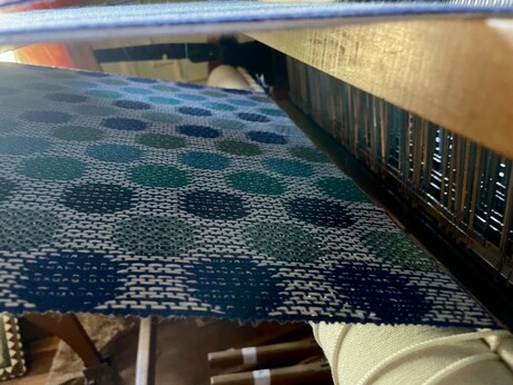 Photo of underside of weaving on the loom. It is white with polka dots of varying blues and greens.