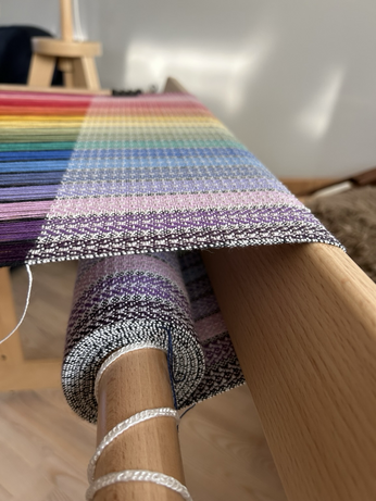 A side look at a hand loom showing woven fabric accumulating around the cloth beam
