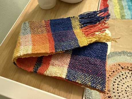 A woven plaid strip of cotton and linen, folded on a cart. It's small and has a fringe, not yet fully trimmed or washed.