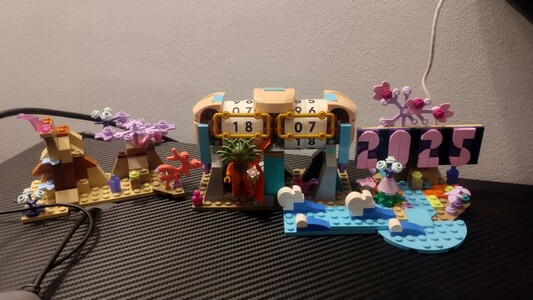 foto de una mesa con tres legos, en uno se ve la fecha de ayer, en otro se lee 2025 y todo tiene un ambiente extraterrestre con plantas moradas