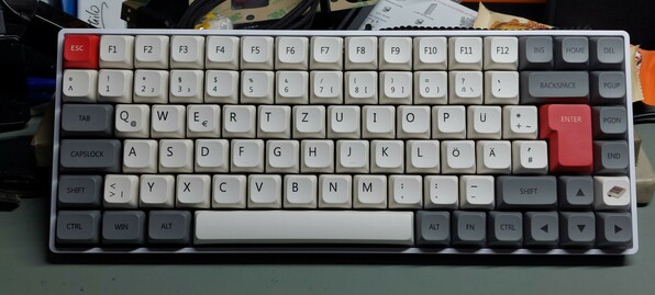 A white 65% keyboard with mostly white keys, with two red and a couple of grey keys as colour accents.
