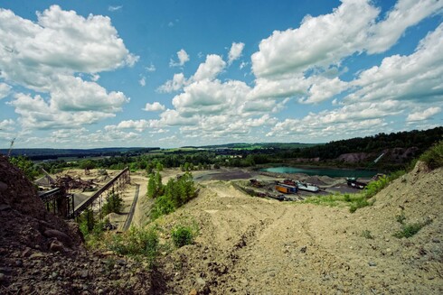 A gravel pit with a pond to the right and a sorting line to the left and dramatic clouds overhead