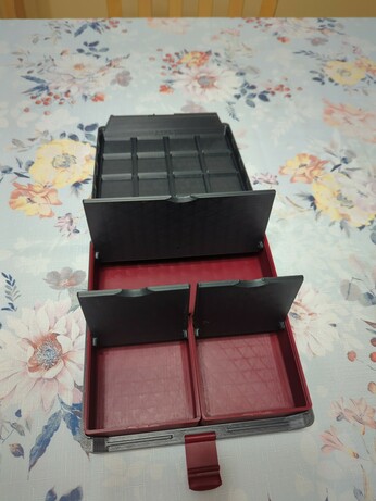 A Gridfinity box, whose outer shell is printed from a dark grey plastic. The inside boxes are a dark red plastic, with dark grey flip lids to match the outer shell. Two boxes are 2 by 2, and one is 4 by 2. All the flip lids are open, as is the main lid. The latch is visible, and it is the same dark red as in the inside boxes.
