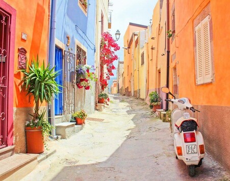 A beautiful stoned street with all different colored old homes lining it!*& Even potted plants and a vintage white scooter parked on the side!