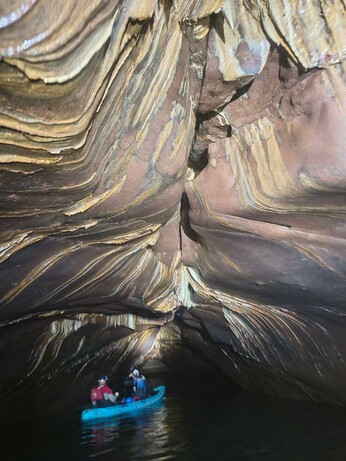 Sea cave chamber with brown sandstone ceiling decorated with pale streaks of speleothem flow-stone.