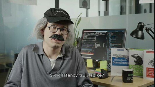An old-school systems engineer in his office,
the subtitles say: "If Grafana chart flickered yellow while no one was watching, did the latency truly spike?"

You can see his monitor with several SSH connections opened, and 3 oreilly books on the table.
The red color book title is "How to move back on-prem", the green color book title is "How to cloud", and the blue color book title is "Introduction to guesstimates"