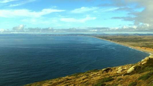 The evening sun providing beautiful light at Point Reyes yesterday. The slopes in the foreground are golden now, rather than the deep green they sported a few months ago. Point Reyes Beach (center right) is colored tan, red, and yellow. Mount Saint Helena appears on the distant horizon, below grey and white clouds set in a light blue  sky. The Pacific Ocean reflects the various colors, from dark blue to  almost blue green, and its surface reveals the effects of wind and waves.