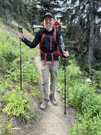 A bearded fellow with a backpack and hiking poles, and very dusty boots