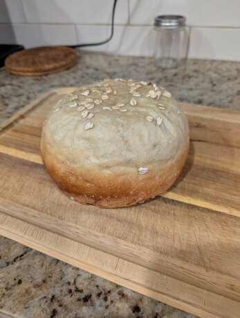 A round loaf of bread with oats on top, resting on a cutting board.